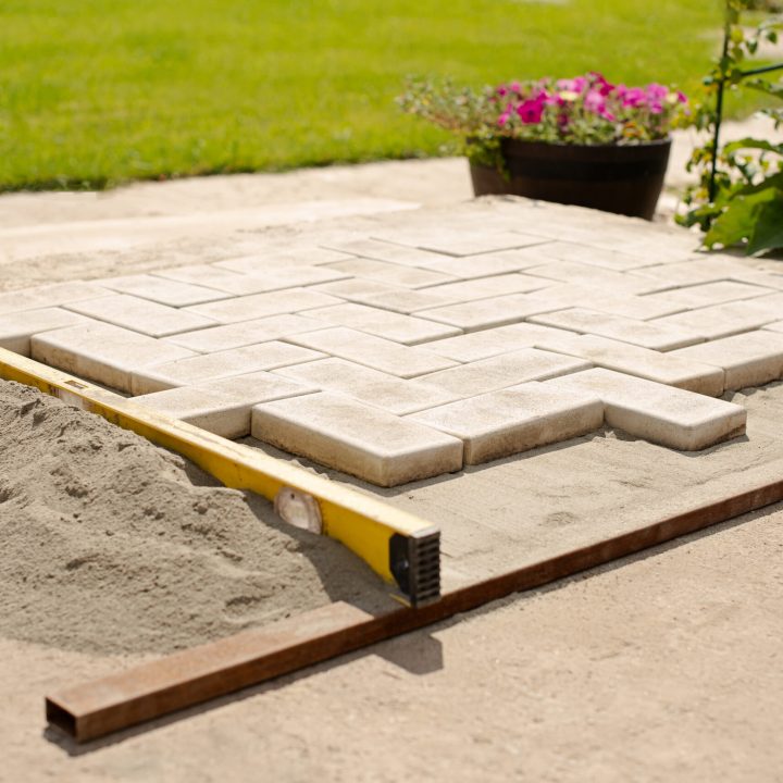 The master lays paving stones in layers. Garden brick pathway paving by professional paver worker. Laying gray concrete paving slabs in house courtyard on sand foundation base.